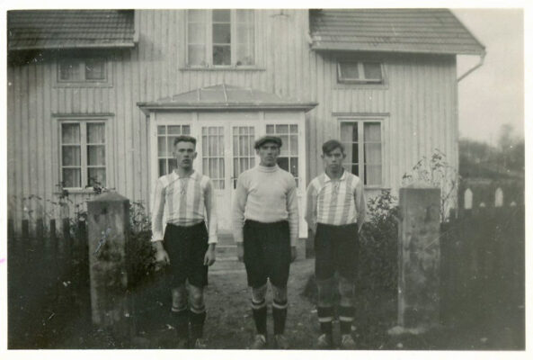 Tre män framför hus