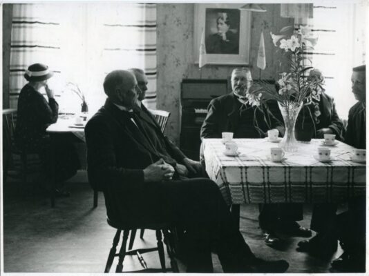 En grupp män runt ett bord. En kvinna i bakgrunden.