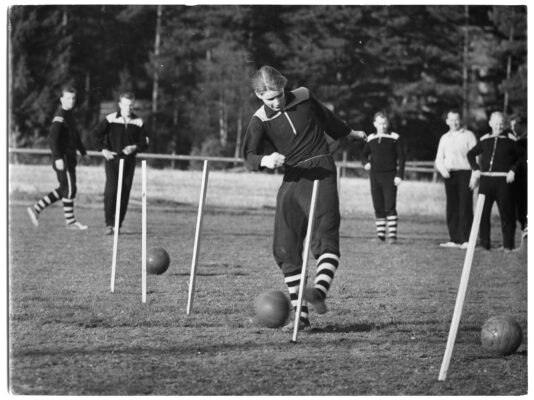 Fotbollsträning. En spelare springer slalomdribblar genom käppar med bollen.