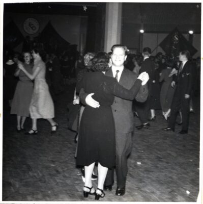 Några dansande par på ett dansgolv. I bakgrunden på väggarna syns fanor.