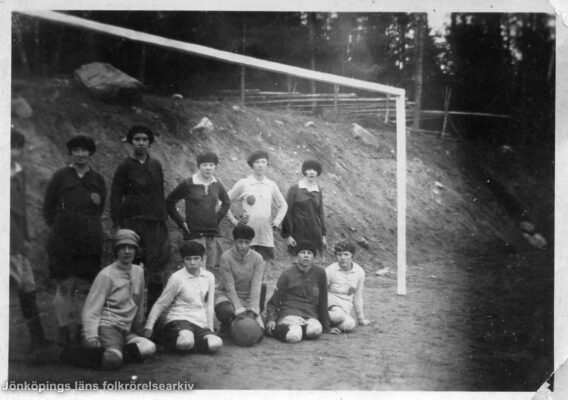 Ett tiotal kvinnor uppställda vid ett fotbollsmål. I bakgrunden en jordvall och längre bort en gärdesgård.