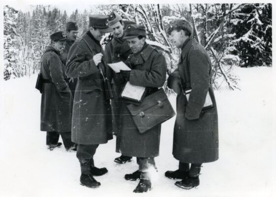 Sju stycken män i militärkläder samlade i en grupp i vinterlandskap.