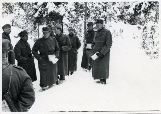 Sju stycken män i militärkläder samlade i en grupp i vinterlandskap.