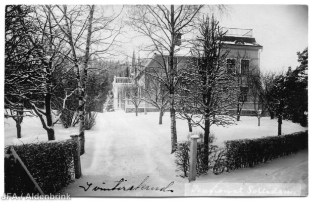 Större byggnad omgiven av snötäckt trädgård.