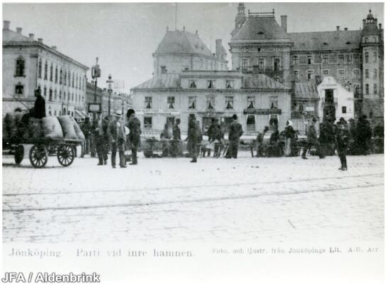 Folksamling och vagn på torg.