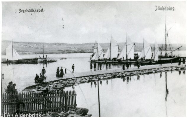 Människor på piren vid ett antal förankrade segelbåtar.