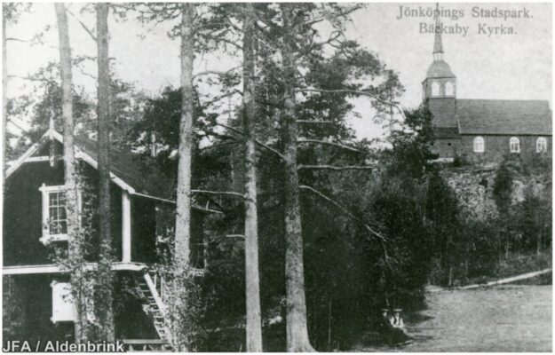 Bäckaby kyrka, äldre trähus, och tallar.