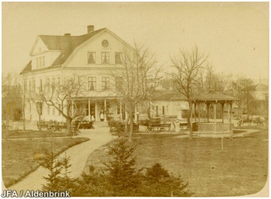 Gult foto av stort hus med paviljong, träd, och många sittplatser. 
