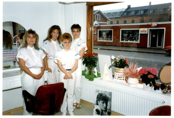 Fyra vitklädda kvinnor inomhus vid en frisörstol. 