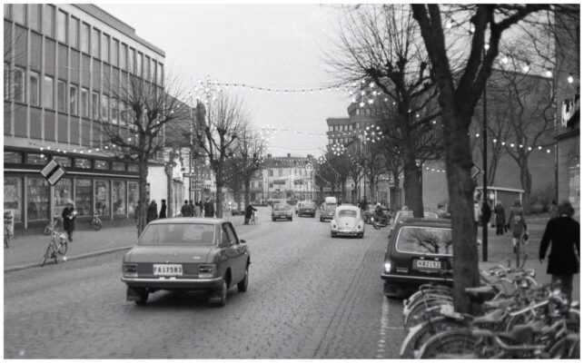Människor, bilar och cyklar i julpyntad stadsmiljö.