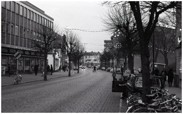 Människor, bilar och cyklar i julpyntad stadsmiljö.