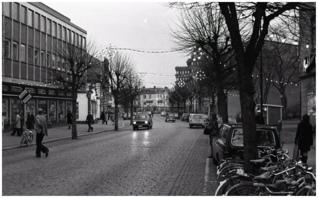 Människor, bilar och cyklar i julpyntad stadsmiljö.