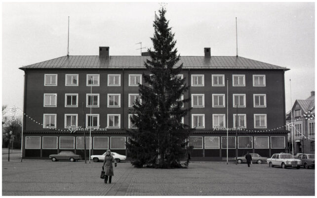 Människor, bilar och cyklar i julpyntad stadsmiljö.