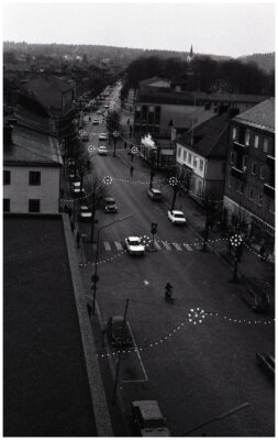 Människor, bilar och cyklar i julpyntad stadsmiljö.