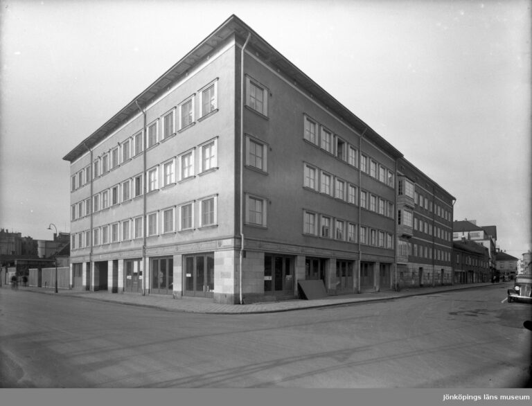 Stort fyrkantigt hus med många fönster vid gatukorsning.