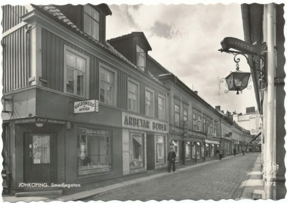 Stengata kantad av trähus, till vänster en guldsmedsbutik och "Arbetarboden" med stor skylt.