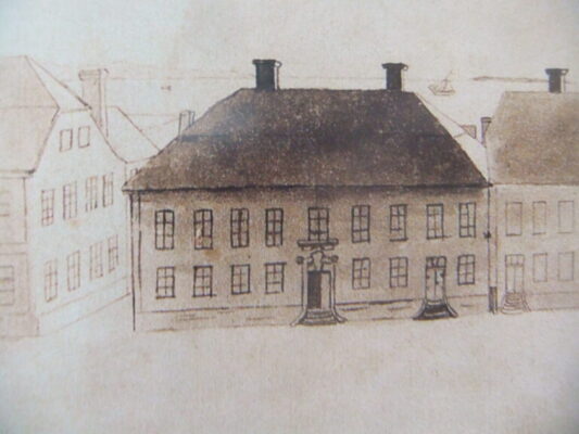 Illustration föreställande tvåvåningshus med många fönster, två entréer, och två skorstenar på ett högt tak, i bakgrunden Vättern med en båt och till sidorna andra mindre detaljerade hus. 