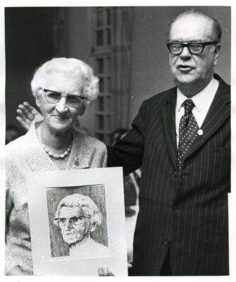 Äldre man och kvinna, kvinnan håller ett porträtt av sig själv.