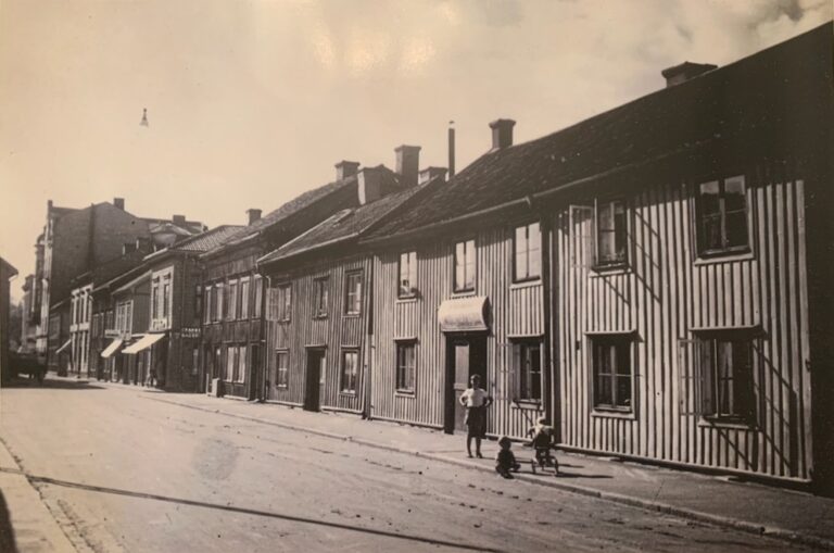 Rad med trähus utmed gata, två eller tre barn på trottoaren.