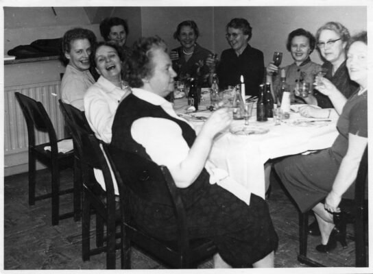 Utklädda och uppklädda damer sitter vid ett bord och har fest.