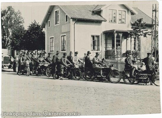 Ett tjugotal personer på motorcyklar på vägen framför en villa.