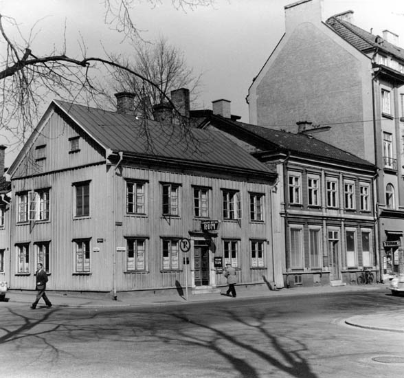 Tvåvånings trähus med skyltning "Rum", samt oläsligt, två gångare.