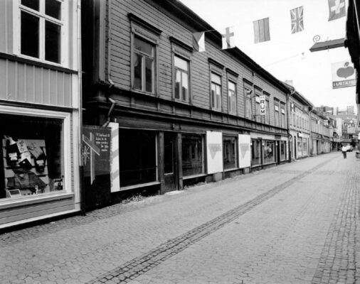 Stengata kantat av trähus, flaggor hänger över gatan. 