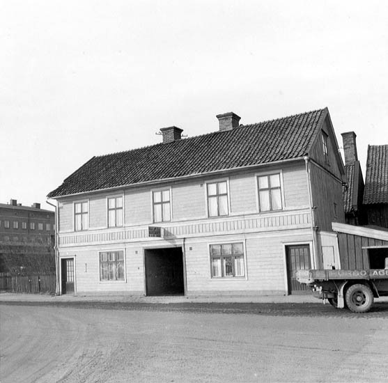 Trähus med stor öppning till innegård, framför är väg med en bil.