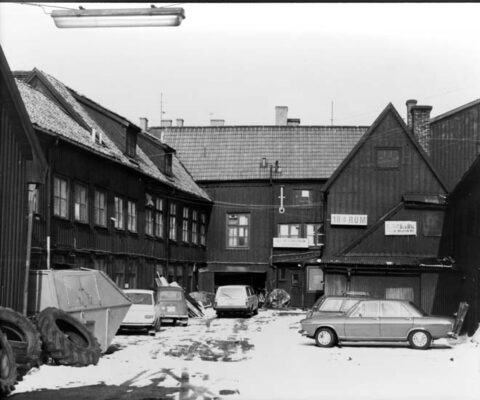 Innegård mellan trähus, flera bilar parkerade och en container. 