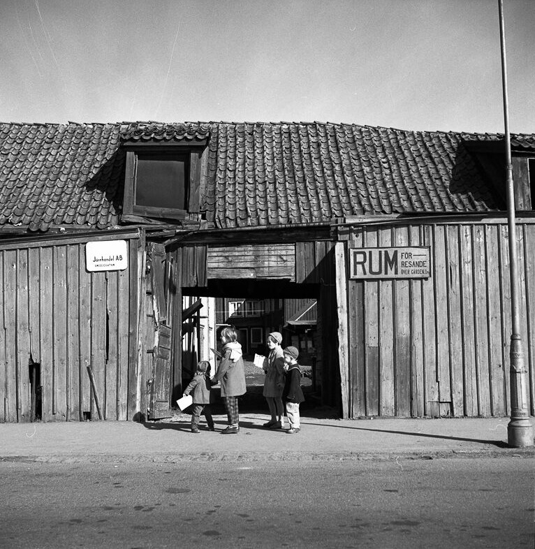 Fyra barn utanför ingången till innegård med skylt "Rum för resande över gården".