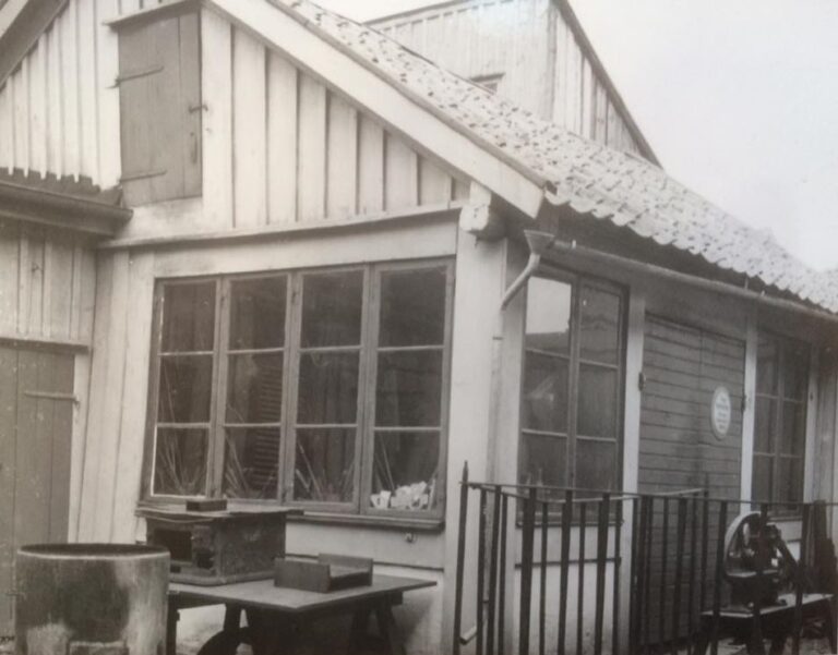 Närbild på trähus med järnstaket och stora fönster.