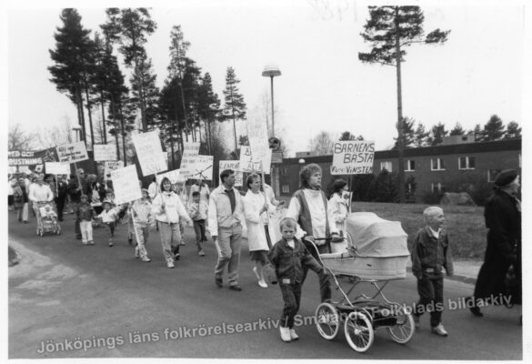 Tåg av folk med skyltar för Barnens Bästa, inklusive barn och barnvagnar. 