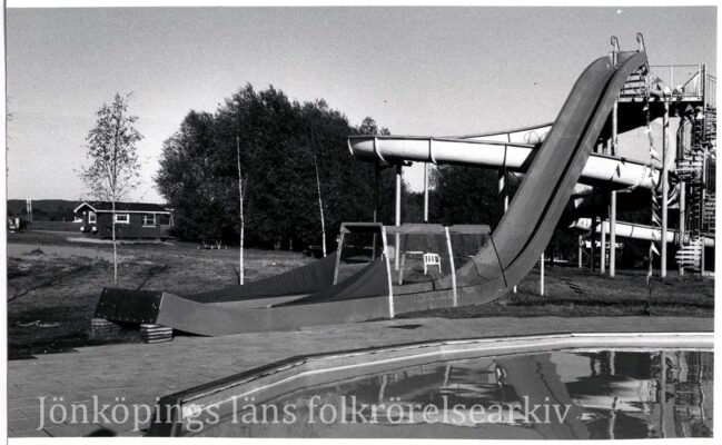 Rutschkanor, bassäng, träd och en stuga.