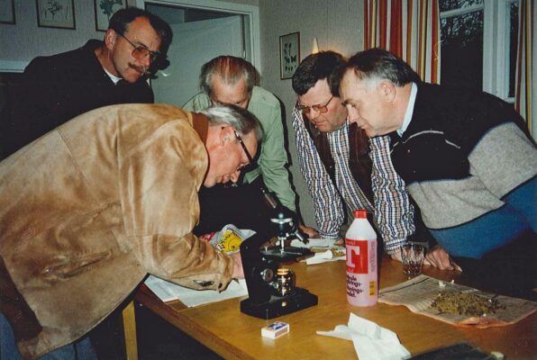 Fem män lutar sig fram över ett bord för att se något.