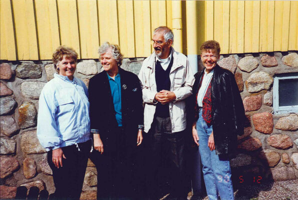 Fyra personer uppställda för fotografering vid en husvägg.