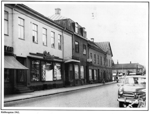 Vy över stadsbebyggelse. I förgrunden del av en bil på en gata.