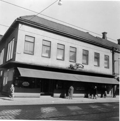 Stenhus med utfälld markis sett från gatan, spårväg utanför.