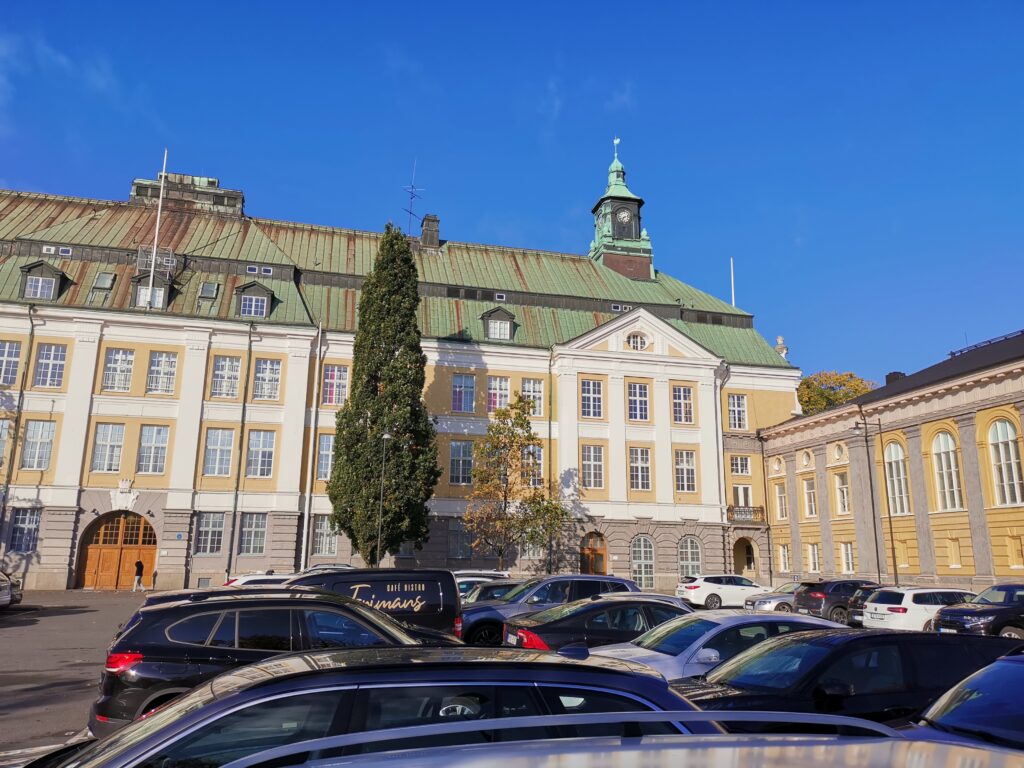 Stor stenbyggnad med parkering i förgrunden.