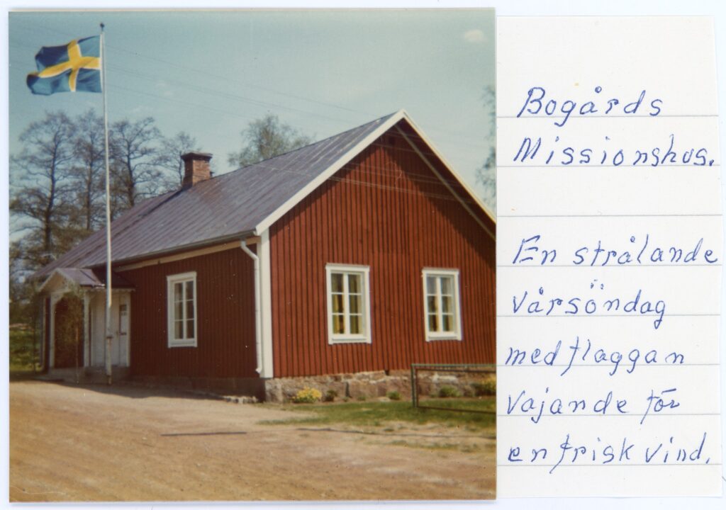 Rött hus med vita knutar och en vajande svensk flagga utanför.