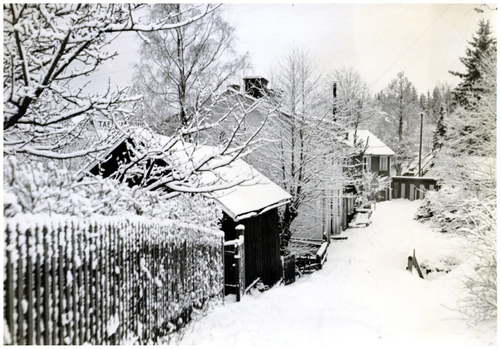 Snötäckt gata med staket, hus och träd.