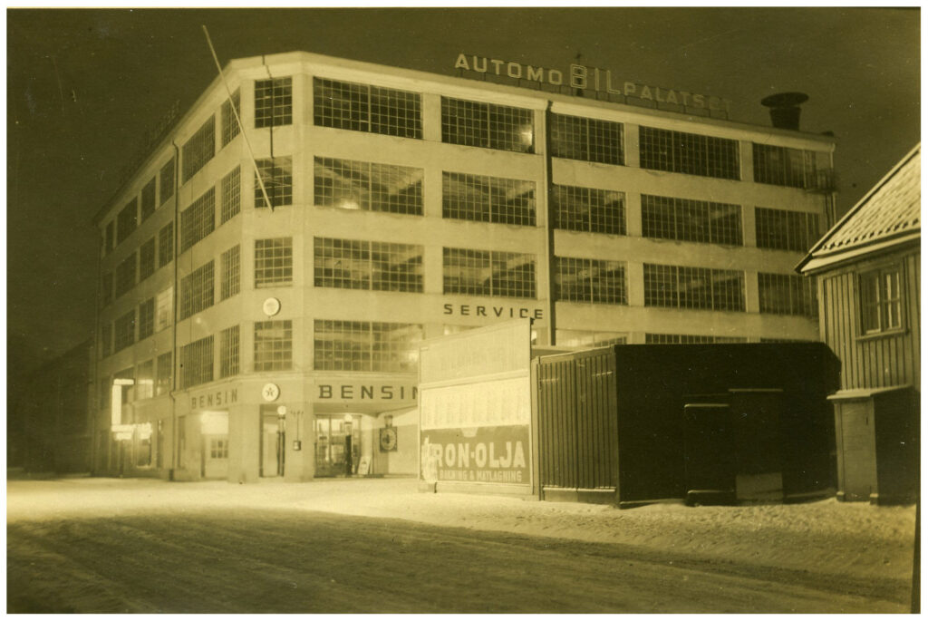 Stor fyrkantig byggnad med skylten "automobilpalatset" med många stora fönster.