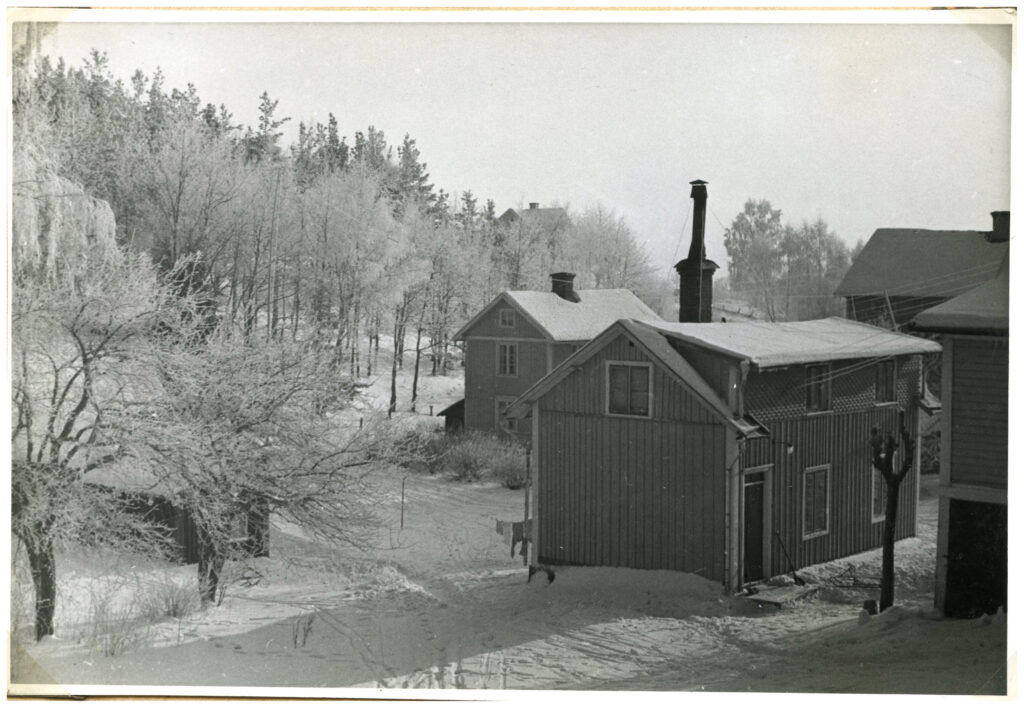 Snötäckt område med några trähus vid skogsparti.