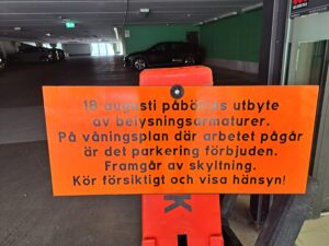 Orange skylt med svart text som upplyser om byte av belysningsarmaturer.