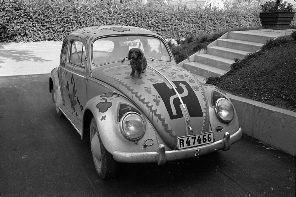 Gammal bil av typ "bubbla" med högertrafiksymbolen och en tax på huven.