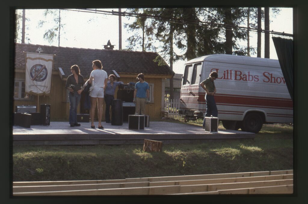 Några personer vid en träaltan med en stor bil med texten "Lill Babs Show".