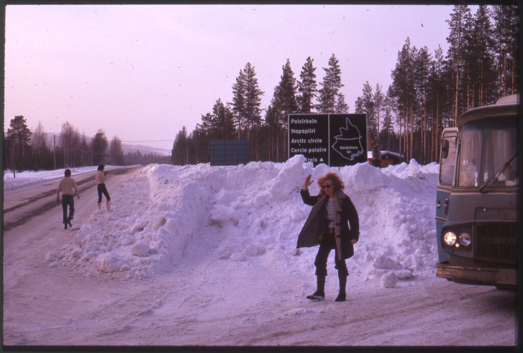 Folkvagn parkerad i snöiga Norrland vid skylt om polcirkeln, tre män utanför.