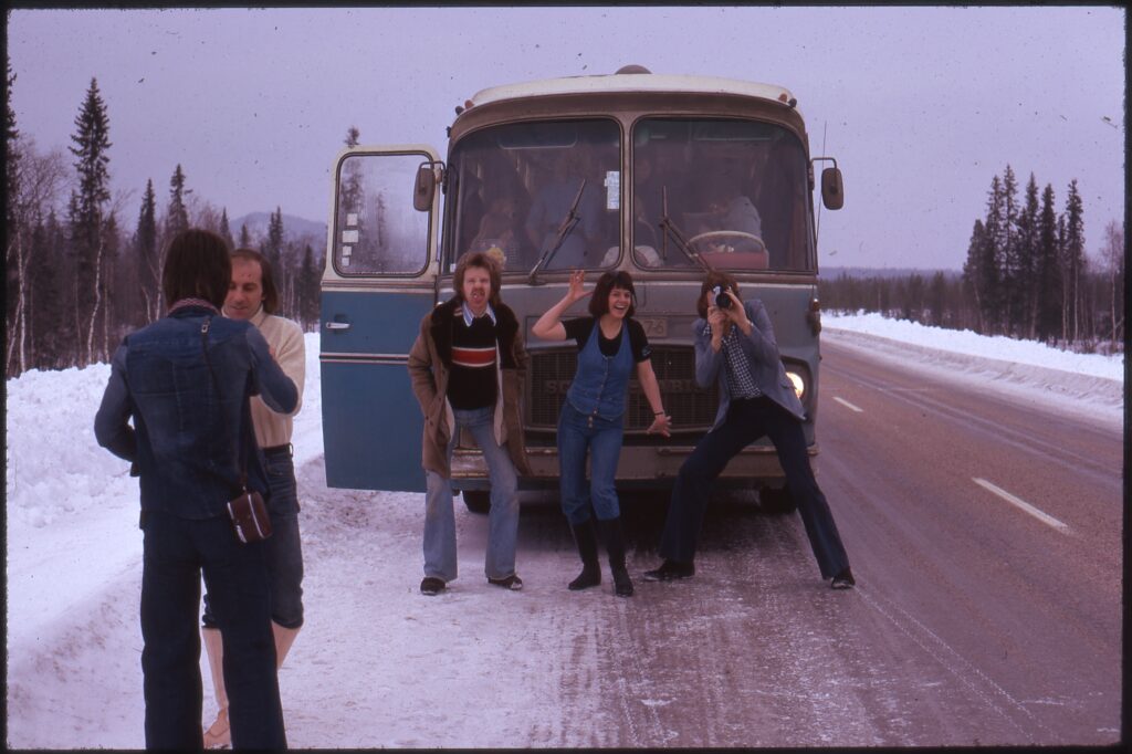 Fyra män och en kvinna utanför en folkvagn på en snöig väg.