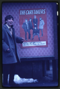 Glad man framför affisch för Caretakers.