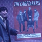 Glad man pekar på affisch med Caretakers.