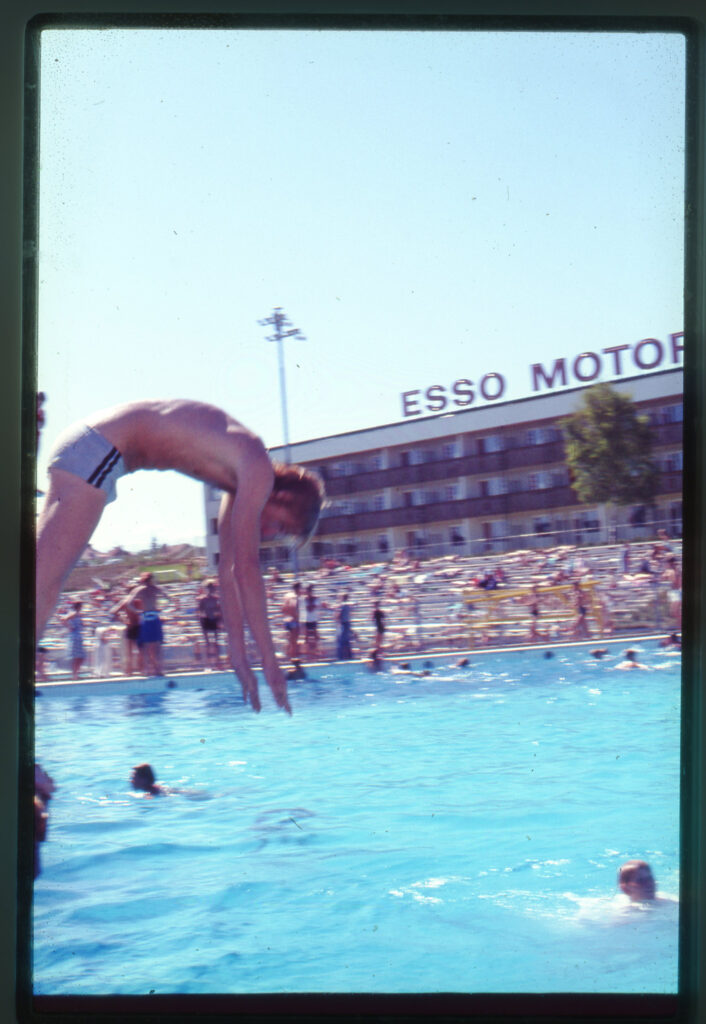 En person dyker ner i en pool framför Esso Motorhotell.